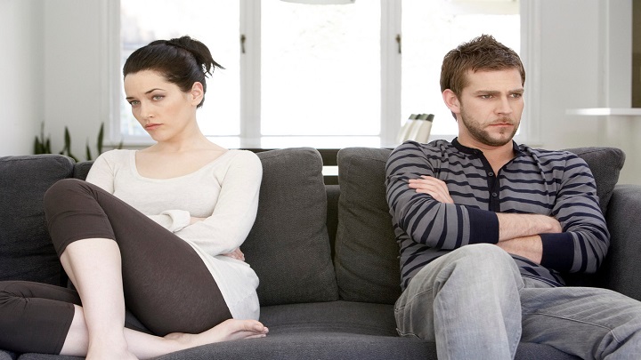 Couple sitting on sofa with arms folded, looking angry