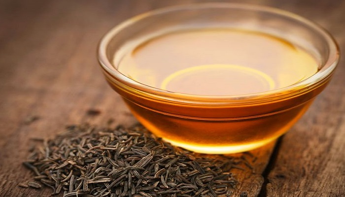 Caraway seeds with essential oil on wooden surface