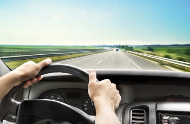 Man's hands of a driver on steering wheel of a minivan car on asphalt road