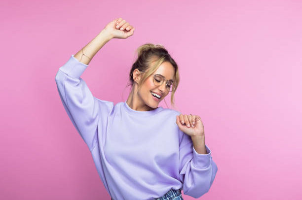 Carefree mid adult woman in casuals dancing against pink background.