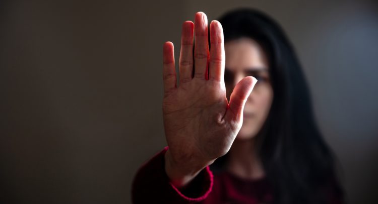 Young woman with raised hand for dissuade. Stop violence against women, sexual abuse, trafficking. Dark room background, copy space.
